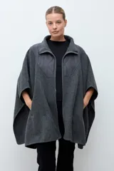 Capa de paño gris con cierre frontal y cuello alto. Presenta un diseño con paneles superiores capitoneados en la zona del pecho y hombros, y aberturas laterales para los brazos.