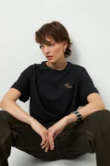 Remera negra de corte oversize con cuello redondo y manga corta. Presenta un pequeño estampado dorado en el pecho con la frase "love earth" y un símbolo de hojas.