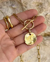 Collar de cadena de eslabones alargados con cierre frontal tipo T y dije circular de textura rústica e irregular.