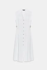 Vestido midi blanco, sin mangas, con cuello solapa y escote pico. Presenta falsos bolsillos con solapas en el pecho, trabillas con hebillas en la cintura y cierre frontal de botones.