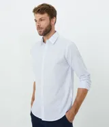 Camisa de corte comfort, manga larga con cuello camisero y cierre frontal de botones. Presenta un estampado de cuadros tipo grid en tonos claros sobre fondo blanco.
