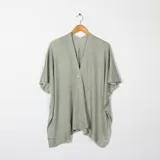Ruana o poncho de tejido de punto fino, color gris verdoso claro, con escote en V y cierre frontal con un botón blanco visible. Presenta mangas cortas tipo murciélago y un calce amplio y asimétrico.