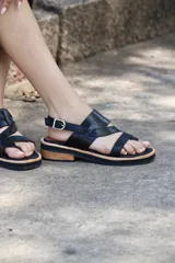 Sandalias bajas de cuero sintético color negro, con tiras cruzadas y hebilla lateral.