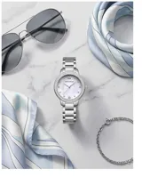 Reloj de pulsera analógico para mujer con caja de metal plateado, bisel decorado con cristales y malla de acero inoxidable. Esfera con fondo nacarado y marcadores de hora con cristales.