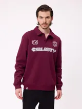 Buzo tipo polo de manga larga color bordó, con cuello camisero y cierre frontal de botones. Presenta estampado gráfico frontal con el número 85, el logo de la marca Rusty y un escudo deportivo.