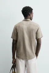 Camisa de lino color beige de corte relajado, con cuello solapa, manga corta y cierre frontal con botones.