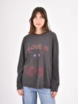 Remera de manga larga en color gris oscuro con efecto lavado. Presenta un estampado frontal con la frase 'LOVE IS HARDCORE' y un diseño gráfico de un corazón con ojos.