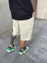 Bermuda de corte baggy en color arena, confeccionada en tejido de algodón resistente, con diseño de cinco bolsillos y cierre frontal con botón y cremallera.