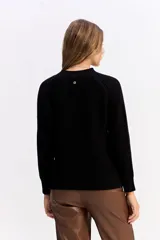 Buzo de punto negro con cuello redondo, manga larga y textura sutil. Presenta un diseño minimalista y versátil, ideal para combinar en diversas ocasiones.