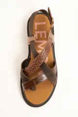 Sandalias de cuero color marrón con suela track, tiras cruzadas en el empeine con diferentes texturas y acabados, y tira ajustable al tobillo con hebilla metálica.