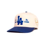 Gorro trucker color beige con visera y detalles bordados en azul que incluyen las letras "LA" y el texto "Mi Casa Su Casa".