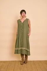 Vestido midi verde militar sin mangas, de corte holgado y silueta acampanada, con cuello en V. Presenta detalles de flecos verticales en el delantero, bolsillos laterales ocultos y una franja inferior con lentejuelas brillantes.