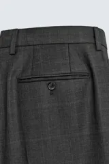 Pantalón de traje de corte regular fit confeccionado en lana de origen italiano. Presenta un diseño de cuadros sutiles, bolsillos laterales, bolsillos traseros de doble vivo con botón y cierre frontal con cremallera y botón.