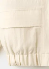 Chaqueta oversize color beige con cuello alto, cierre frontal de cremallera, bolsillos frontales con solapa y mangas largas.