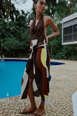 Falda midi de corte cruzado con diseño tipo pareo, presenta un nudo decorativo en la parte delantera y cierre de cremallera oculta en la espalda. El tejido cuenta con un estampado geométrico abstracto en tonos bordó, negro, amarillo y crema.