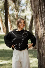 Buzo de punto color negro con diseño de bordado en hilo crudo que forma líneas curvas decorativas. Presenta cuello redondo, mangas largas con caída relajada y corte holgado.