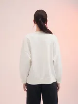 Buzo blanco de corte clásico con estampa rectangular centrada en el frente con flores rosadas y texto en color ocre.