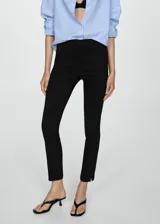 Pantalón negro de corte ajustado y tiro medio, con bolsillos laterales y cierre frontal con cremallera y botón.
