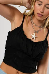 Top negro con breteles finos, escote recto con frunce y corte crop.