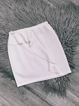 Minifalda blanca de tela crepe con cintura elastizada y volado diagonal en el frente.