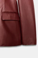 Blazer cruzado de efecto piel color bordó, con solapas de muesca, mangas largas y bolsillos con solapa en la parte delantera. Cierre frontal con botones a tono.