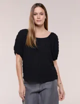 Blusa negra con textura en relieve, escote cuadrado y mangas cortas abullonadas con elástico en los puños, de silueta relajada y fluida.