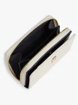 Billetera compacta Tommy Hilfiger color beige, con textura y monograma TH en bajo relieve. Cuenta con cierre de cremallera y detalle metálico del monograma en la parte frontal.