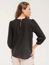 Blusa blanca de algodón con escote redondo, manga tres cuartos y silueta oversized. Presenta bordados y texturas combinadas.