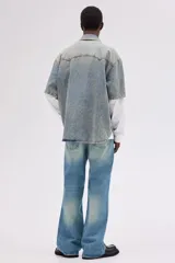 Jean de cinco bolsillos en denim de algodón rígido, tiro alto, con cierre y botón. Corte estándar con pierna acampanada amplia. Presenta un lavado celeste claro con efecto degradado o tie-dye en la parte inferior de las piernas.