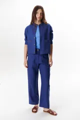 Pantalón de lino color marrón oscuro, tiro alto, corte recto y holgado, con pinzas delanteras y pespuntes a contratono en blanco.