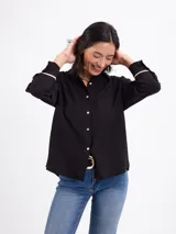 Camisa de manga larga color malva, con cuello clásico, cierre frontal con botones y detalles de vivos negros en los puños.