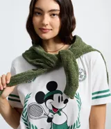 Remera blanca de algodón con cuello redondo y mangas cortas. Presenta un estampado frontal de Mickey Mouse con temática de tenis y detalles de rayas verdes en las mangas.