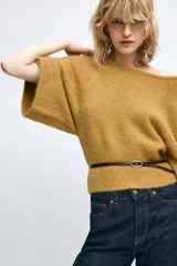 Jersey de punto color mostaza con cuello redondo y mangas amplias tipo murciélago. Presenta un diseño ajustado en la cintura con un cinturón fino de cuero sintético en color marrón a contraste.