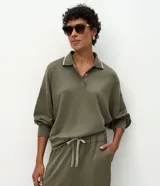 Buzo cerrado de corte holgado confeccionado en tejido de viscosa y poliéster, color verde oliva. Presenta cuello polo con detalle de línea contrastante en el borde, cierre frontal parcial con botones y mangas largas con puños ajustados.