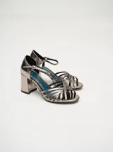 Sandalias de taco alto ancho con diseño retro, confeccionadas en charol negro. Presentan tiras delanteras múltiples entrelazadas, talón cerrado y una correa fina ajustable al tobillo con hebilla metálica.