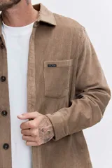 Camisa de pana color tostado, con cuello clásico, cierre frontal de botones y bolsillo en el pecho con etiqueta pequeña.