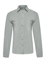 Blusa de manga larga con cuello camisero, confeccionada en una mezcla técnica de algodón orgánico, nylon y spandex. Presenta cierre frontal con botones, dos bolsillos frontales con solapa y paneles laterales reforzados. Cuenta con protección solar UPF 20+ integrada.