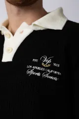 Sweater de punto con textura waffle en color blanco, con cuello polo en contraste color verde oscuro y cierre frontal de botones. Presenta un bordado decorativo en el pecho y un corte relajado.