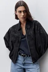 Campera marrón de poliuretano con acabado texturizado, silueta relajada, cuello camisero, cierre frontal, hombros caídos y mangas amplias con efecto abombado.