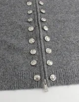 Cardigan de punto gris con cuello alto, cierre frontal de cremallera y doble hilera de botones decorativos metálicos. Diseño de manga larga y corte recto.
