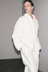 Sobrecamisa blanca de algodón con cuello solapa, manga larga y dos bolsillos de plastrón en el pecho. Cierre frontal con botones ocultos por solapa.