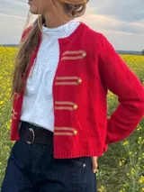Cardigan rojo de punto, con diseño de inspiración militar, cuello redondo, manga larga y cierre frontal decorado con tiras horizontales beiges y botones dorados metálicos con relieve.