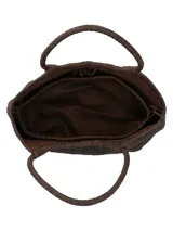 Bolso tipo tote de mimbre trenzado color marrón oscuro, con doble asa superior y parche de cuero con logo de la marca en el frente.