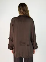 Camisa de satén color negro con cuello mao y volados en las mangas. Presenta cierre frontal con botones y diseño de corte holgado con largo asimétrico.