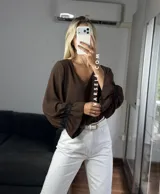 Blusa de tela cey color bordó, con escote en V y mangas largas abullonadas que terminan en puños con detalle de encaje y volados.