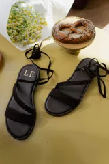 Sandalias bajas de cuero color marrón, con tiras finas para atar alrededor del tobillo.