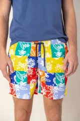Short de baño de secado rápido con cintura elástica y cordón ajustable. Presenta un diseño de patchwork con bloques de colores vibrantes (amarillo, rojo, azul, verde azulado, celeste) y estampado floral blanco en cada bloque.