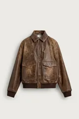 Cazadora de piel marrón con acabado efecto vintage, corte relaxed fit, cuello solapa y cierre frontal con cremallera oculta. Cuenta con bolsillos de plastrón con solapa en la parte delantera y acabados de rib elástico en puños y cintura.