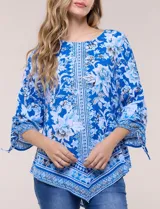 Blusa de gasa azul con estampado floral y geométrico estilo pañuelo, escote redondo, mangas tres cuartos amplias con jareta ajustable y ruedo asimétrico en punta.