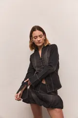 Camisa de jean color negro con efecto lavado, de manga larga con puños acampanados y cierre frontal mediante cordones trenzados. Presenta costuras a la vista en color blanco.